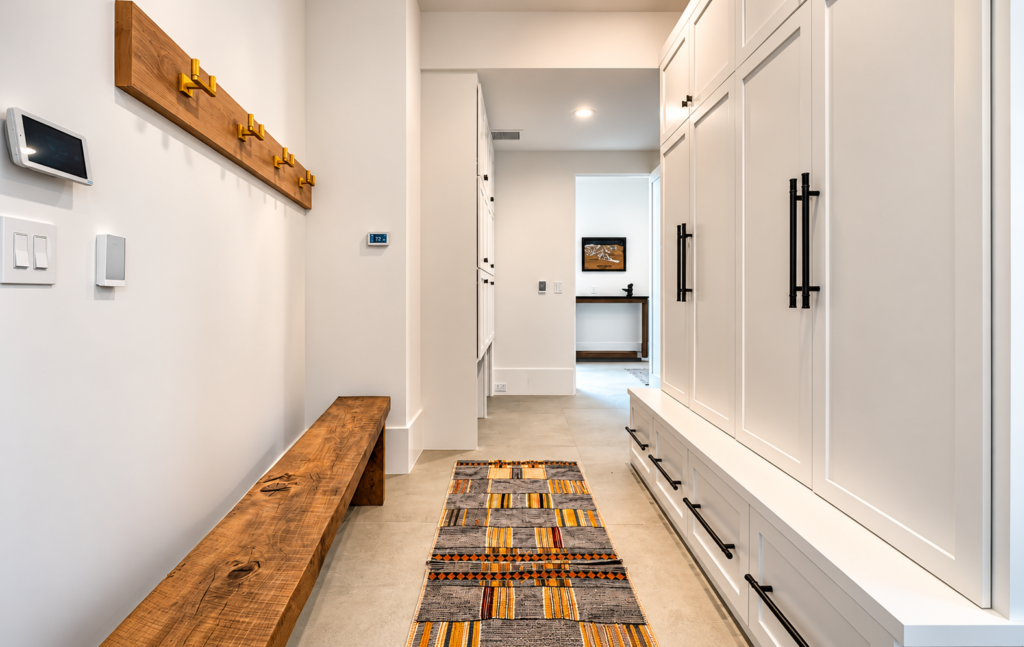 Modern mudroom in a Steamboat Springs luxury home featuring white built-in storage cabinets, a natural wood bench, brass coat hooks, and patterned runner rug.