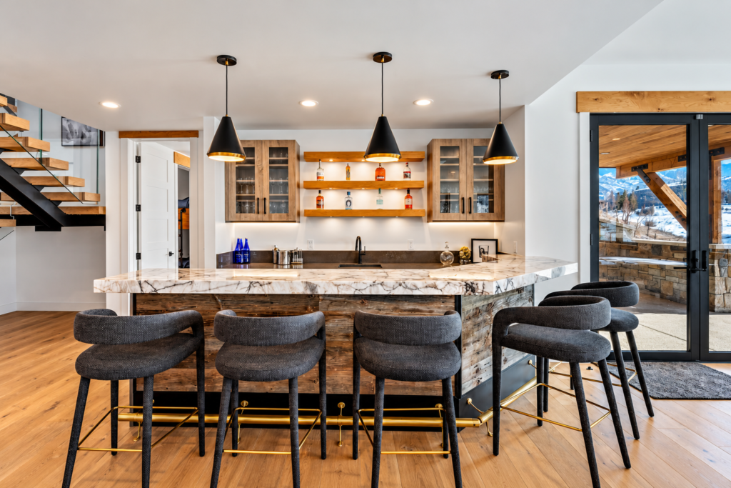 Contemporary entertainment bar in a Steamboat Springs luxury home featuring a marble countertop, rustic wood cabinetry, pendant lighting, and upholstered bar stools.