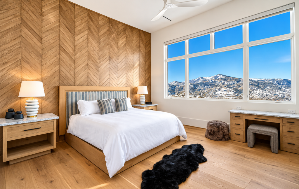 Modern luxury bedroom in Steamboat Springs, Colorado, featuring a chevron wood accent wall, natural oak flooring, and expansive windows overlooking snow-covered mountains.