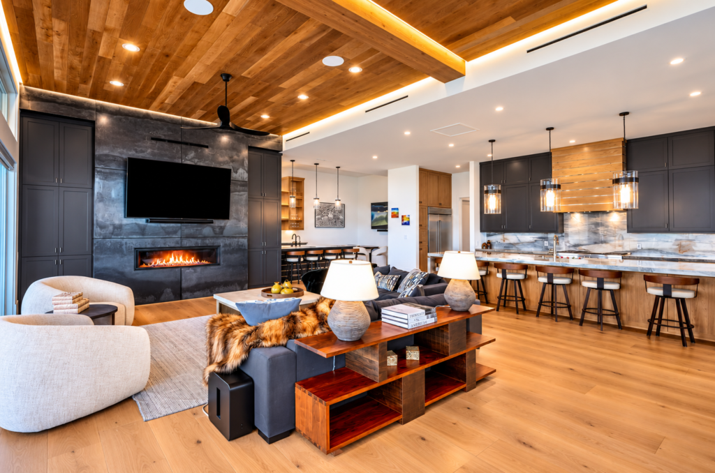 Open-concept kitchen and living room in a Steamboat Springs luxury home featuring a wood ceiling, modern fireplace, marble countertops, and contemporary cabinetry.